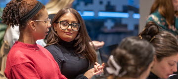 Fyra unga kvinnor som sitter och samtalar över några böcker och ser glada ut 