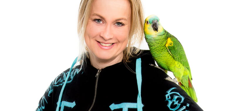En ljushårig kvinna i svart hoodtröja med en papegoja på sin axel.