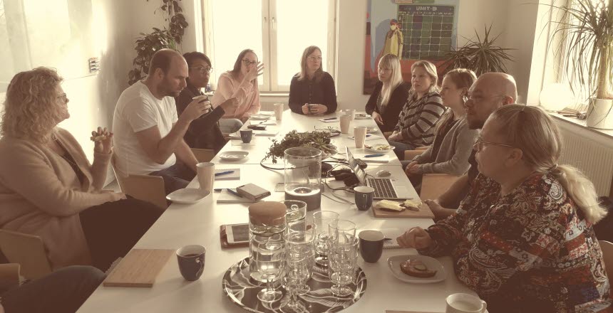 Ett tiotal personer som sitter kring ett konferensbord och samtalar och fikar