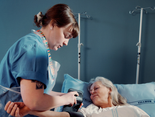 Sjuksköterska tar blodtryck på sängliggande kvinnlig patient. 