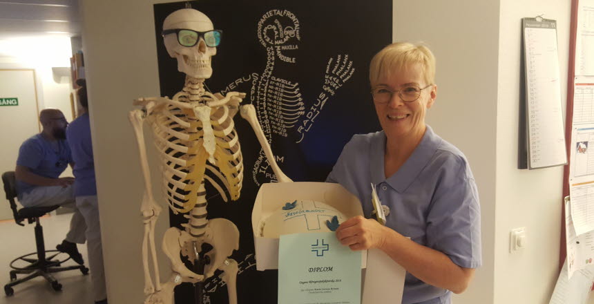Karin Larsson Bylund, dagens röntgensjuksköterska, i händerna har hon en tårta i kartong och ett diplom. Bredvid henne står ett skelett med glasögon på sig.