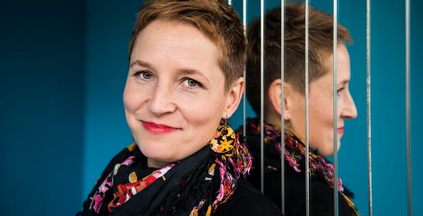 Sara Heyman en korthårig kvinna med rött läppstift lutar sig moten spegel där man ser hennes spegelbild