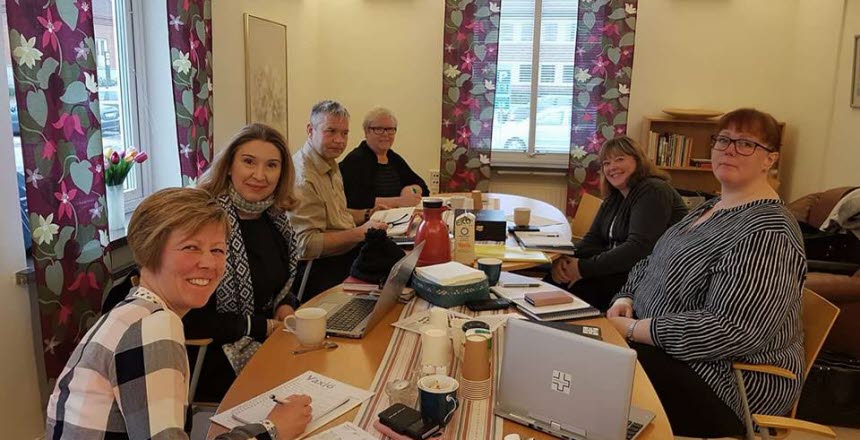 Det sitter 6 personer kring ett konferensbord med datorer och kaffe på bordet