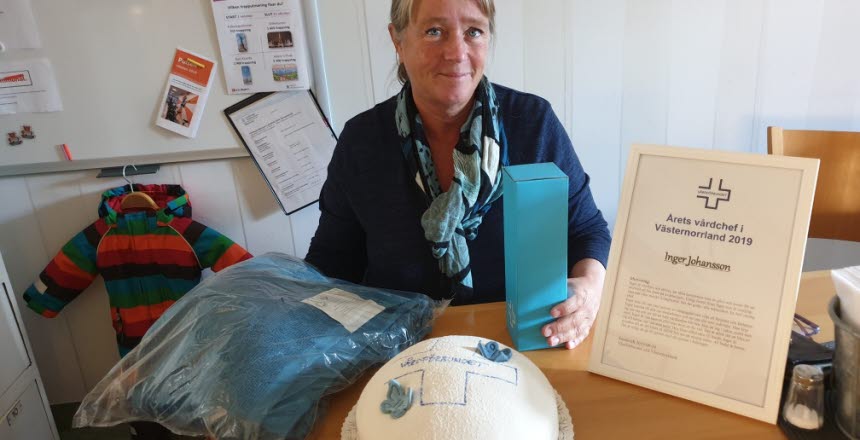 Årets vårdchef Inger Johansson sitter vid ett bord med ett diplom och en tårta framför sig
