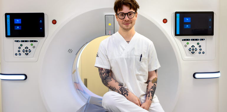 Röntgensjuksköterska med mörkt hår och vita kläder hjälper en patient  som ligger på en brits in i magnetröntgen